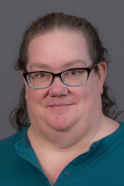 White woman with dark hair infront of a dark grey background
