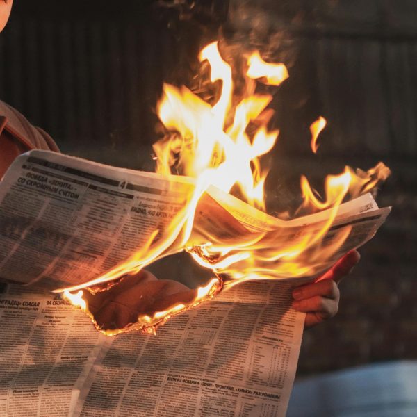 Hands holding a burning newspaper against a dark, blurred background.