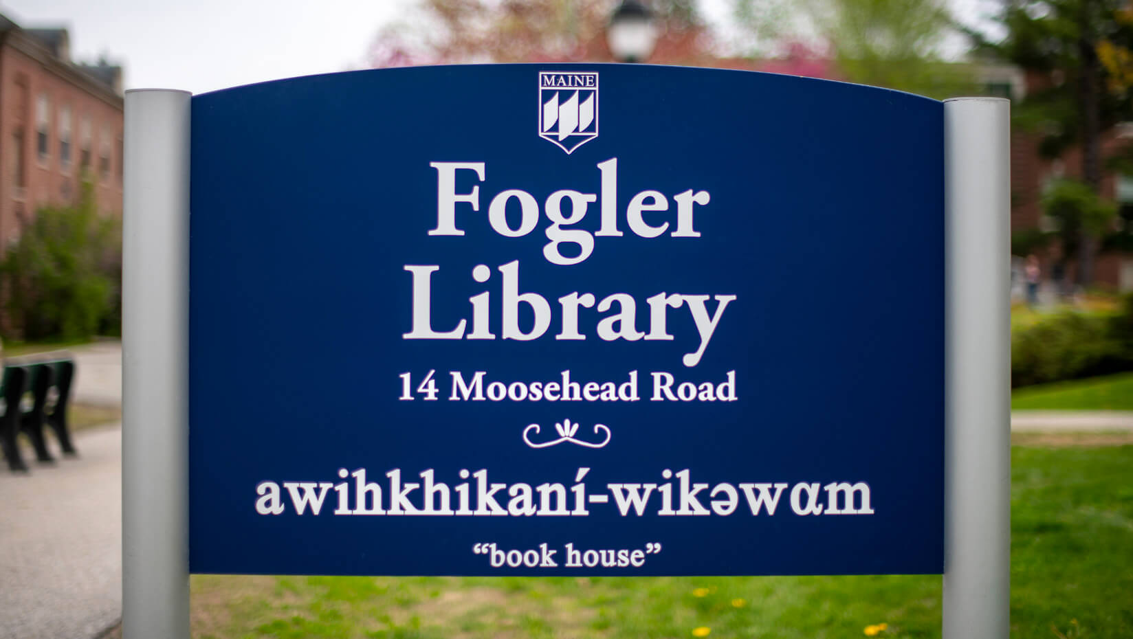 Sign for Fogler Library at the University of Maine. The sign is blue with white text, featuring the library name, address, and the phrase "awihkhikani-wikәwam" which translates to "book house" underneath.