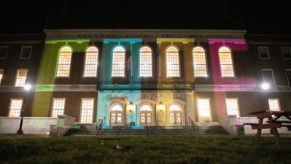 Fogler at night, with CARE projected onto building with multi-colored lights.