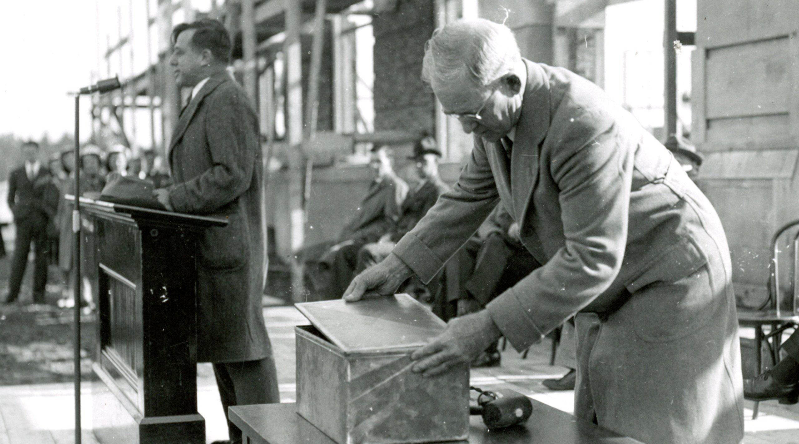 Arthur Hauck speaking while another man closes a time capsule to place in the library cornerstone