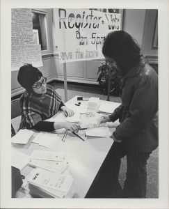 A woman at a table assisting a student in registering to vote in 1971