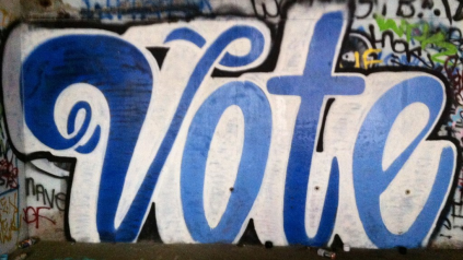 The word vote spraypainted on a white wall.